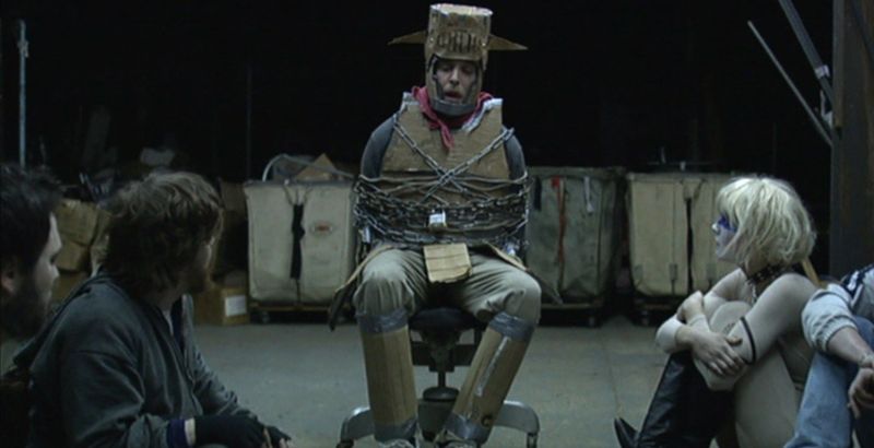 man in cardboard armor tied to a chair from murder party